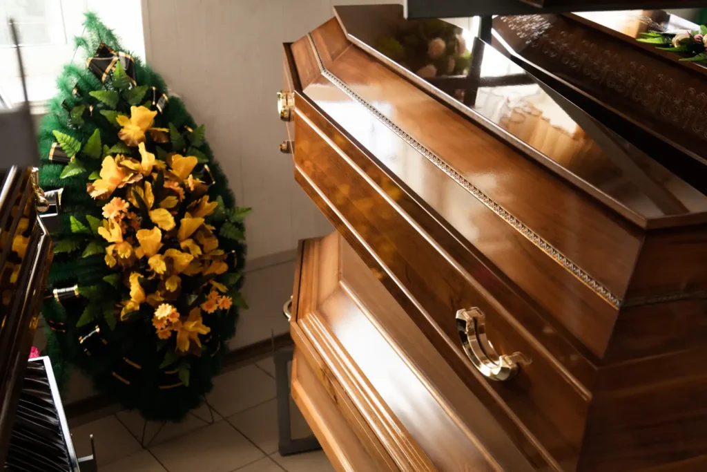 Several caskets stacked on top of one another in a rack next to a large wreath of flowers