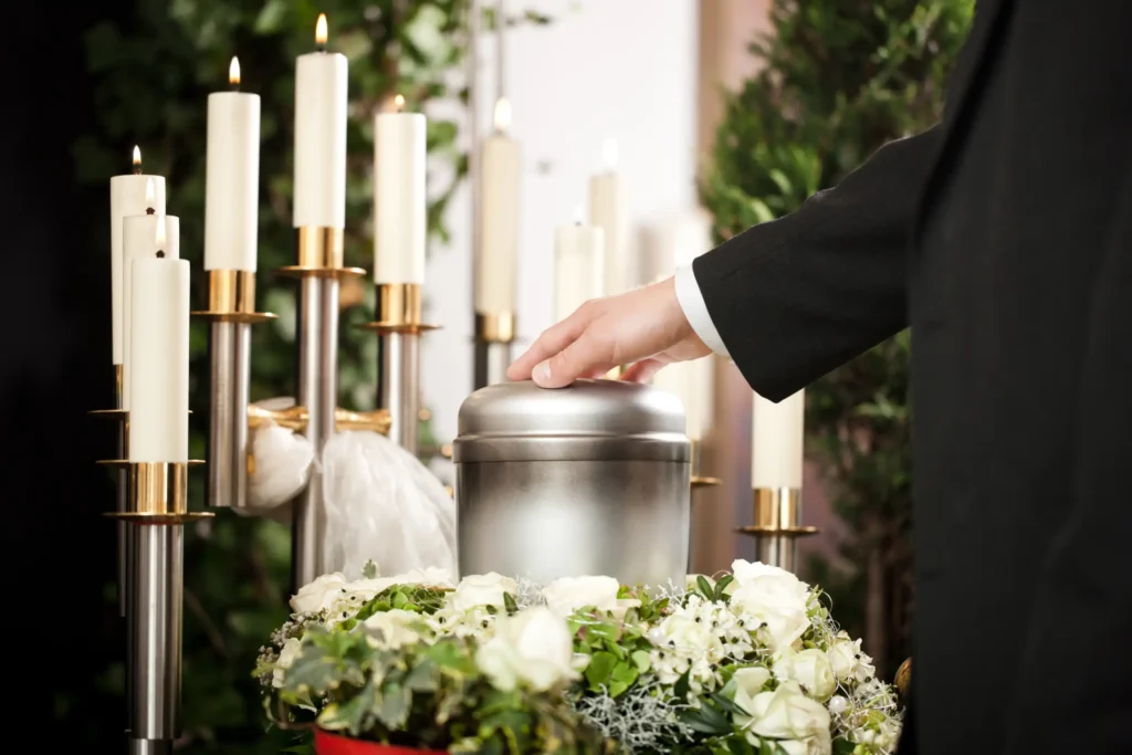 A mourner touching the lid of a silver, cylindrical urn placed in front of a row of candles in a church