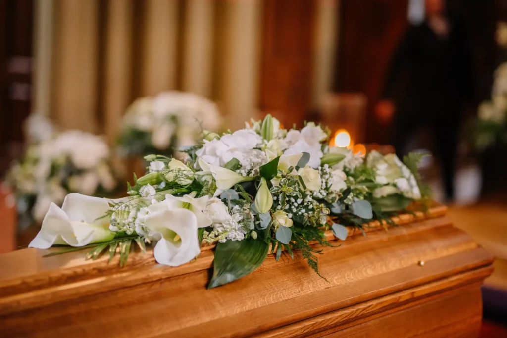A light brown casket with a bouquet of white flowers atop it inside a church